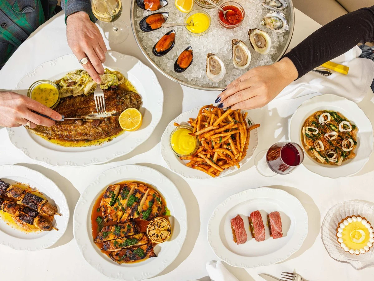 A spread of dishes from Crevette with hands taking the Dover sole and a frite at Sip & Guzzle.