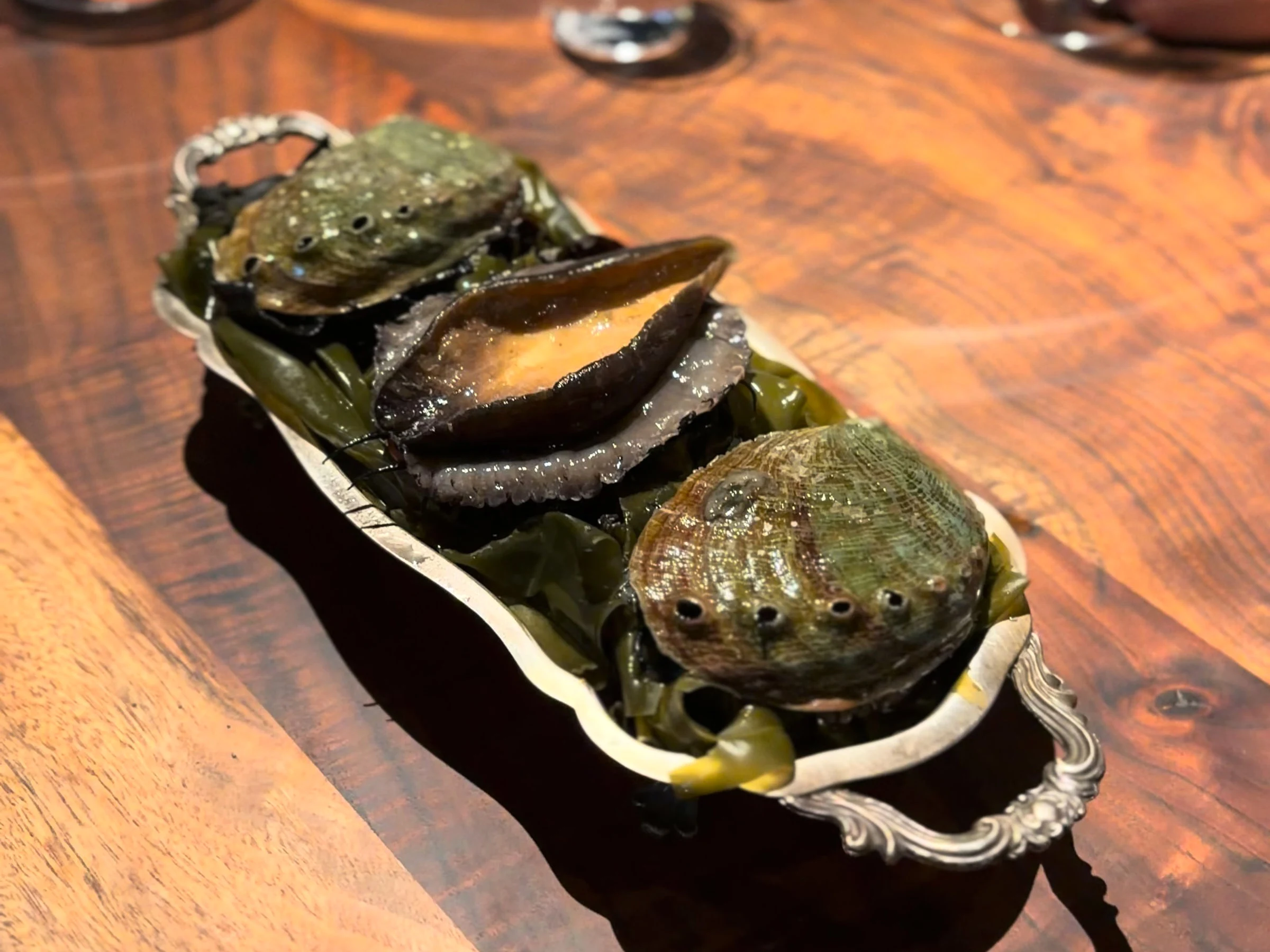 Whole abalone and shells presented on seaweed in a silver handled tray at Saison