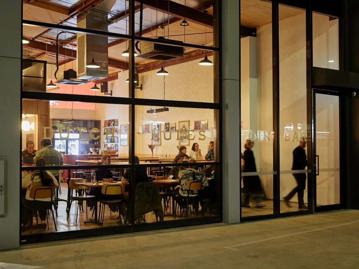 Night-time exterior shot of Dutch Rules distillery/restaurant on Whitehorse Road, Mitcham, showing the large black-framed glass shopfront with 'DUTCH 
