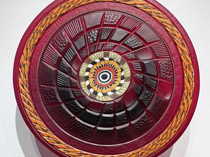 A circular glass art piece by Davide Salvadore, featuring intricate murrine patterns in concentric rings of burgundy, gold, and orange, with a