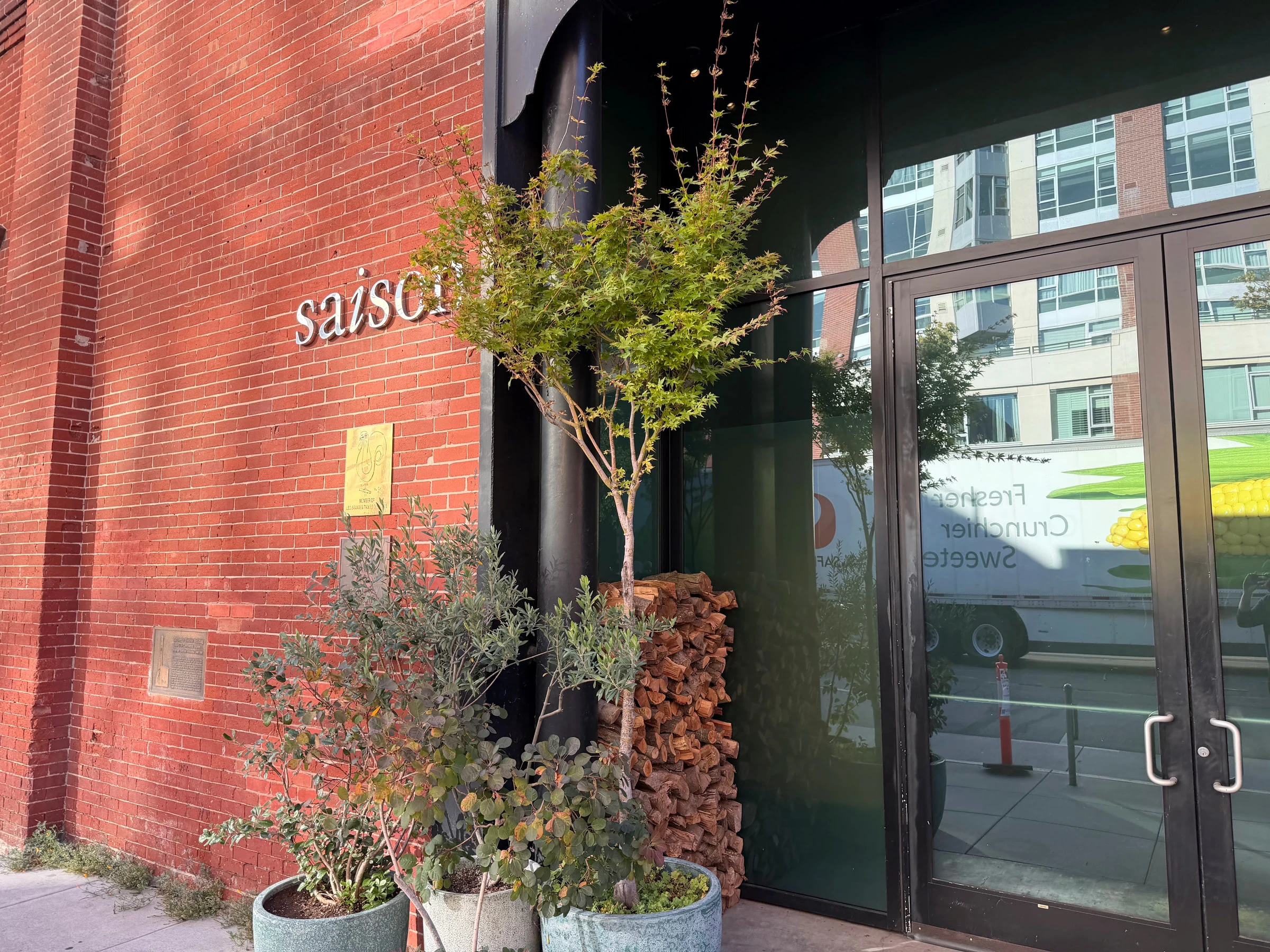 Saison restaurant entrance on Townsend Street with a brick facade, leafy planters, and stacked almond firewood