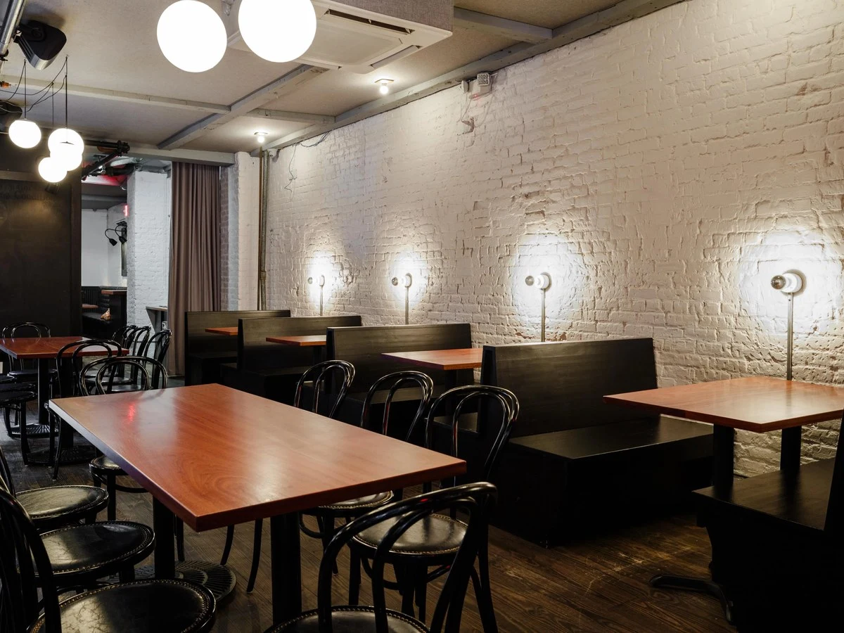 Interior of Existing Conditions bar with white brick walls, dark wooden tables, black chairs, and globe lights.