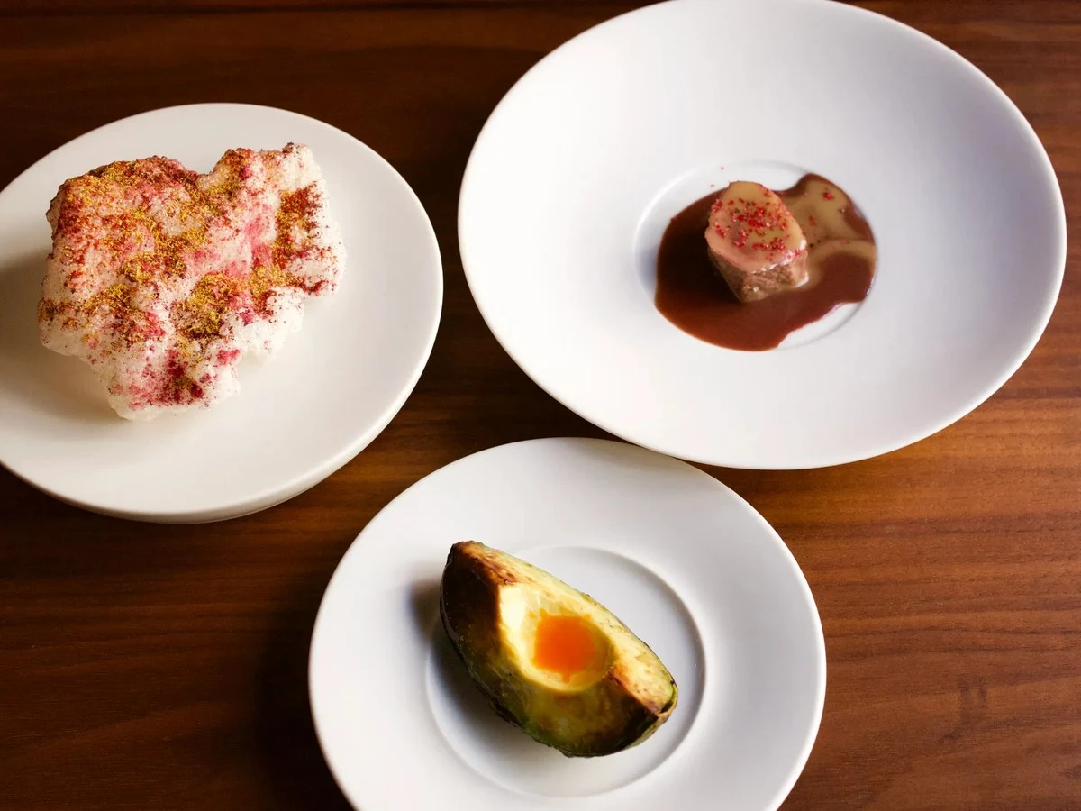 Three plated Saison courses on white dishes, including a venison course, photographed from above on a wooden table.