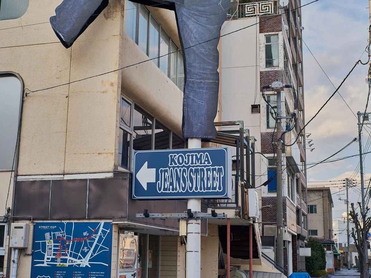 A giant denim jeans sculpture tops a signpost pointing to Kojima Jeans Street, with a detailed street map below.