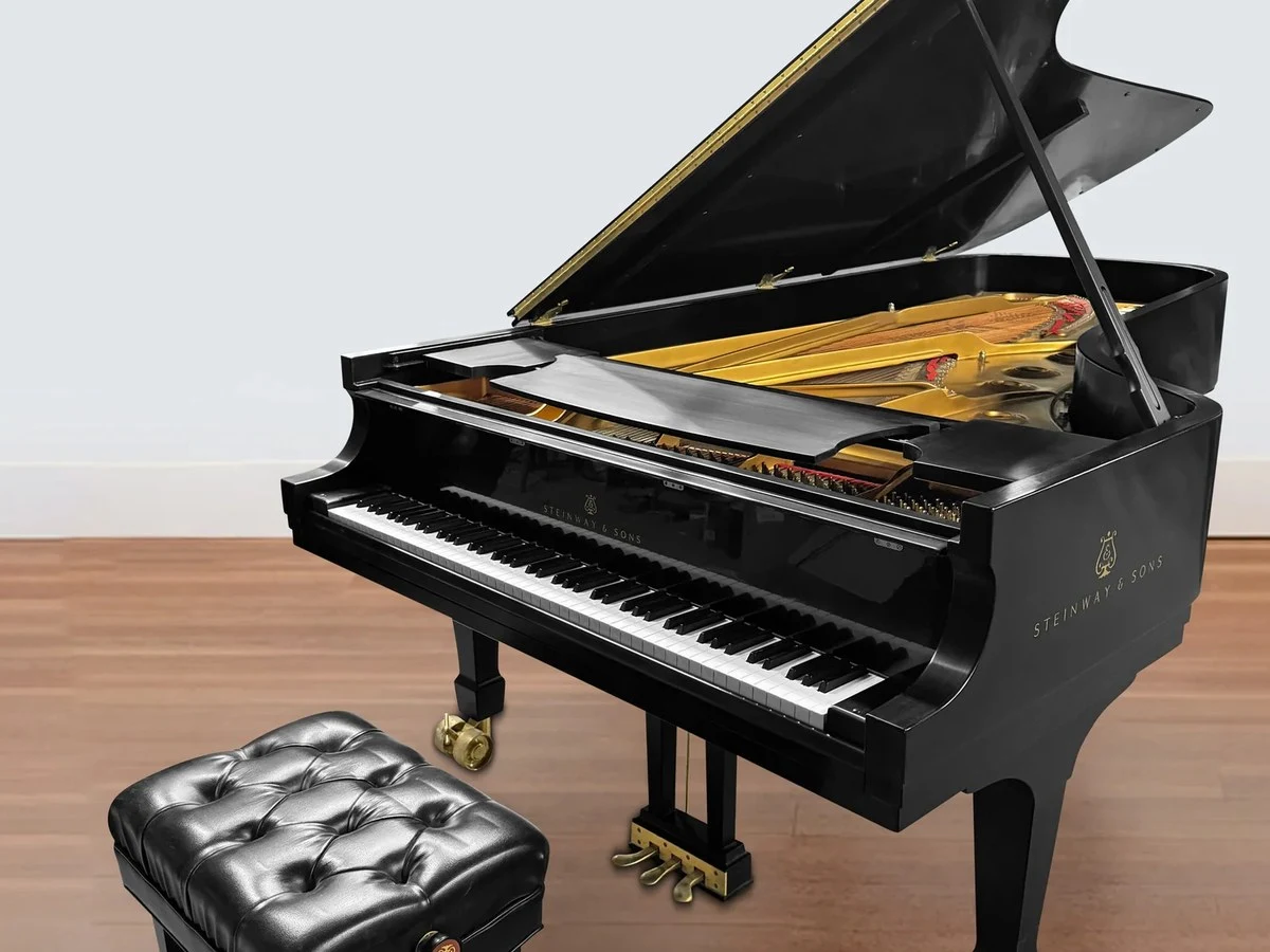 Steinway & Sons: A Model D Concert Grand piano, its lid open to reveal golden strings, with a tufted bench.