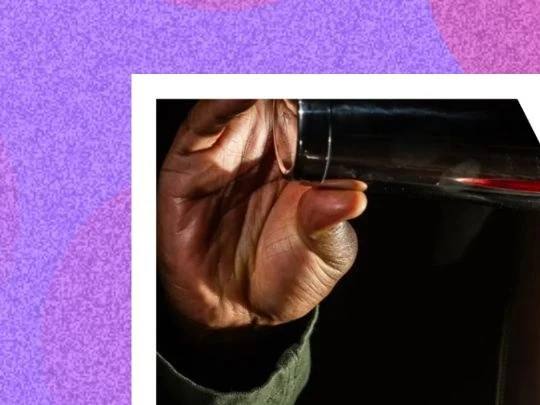 Close-up of a person's hand holding a dark glass bottle against a black background.