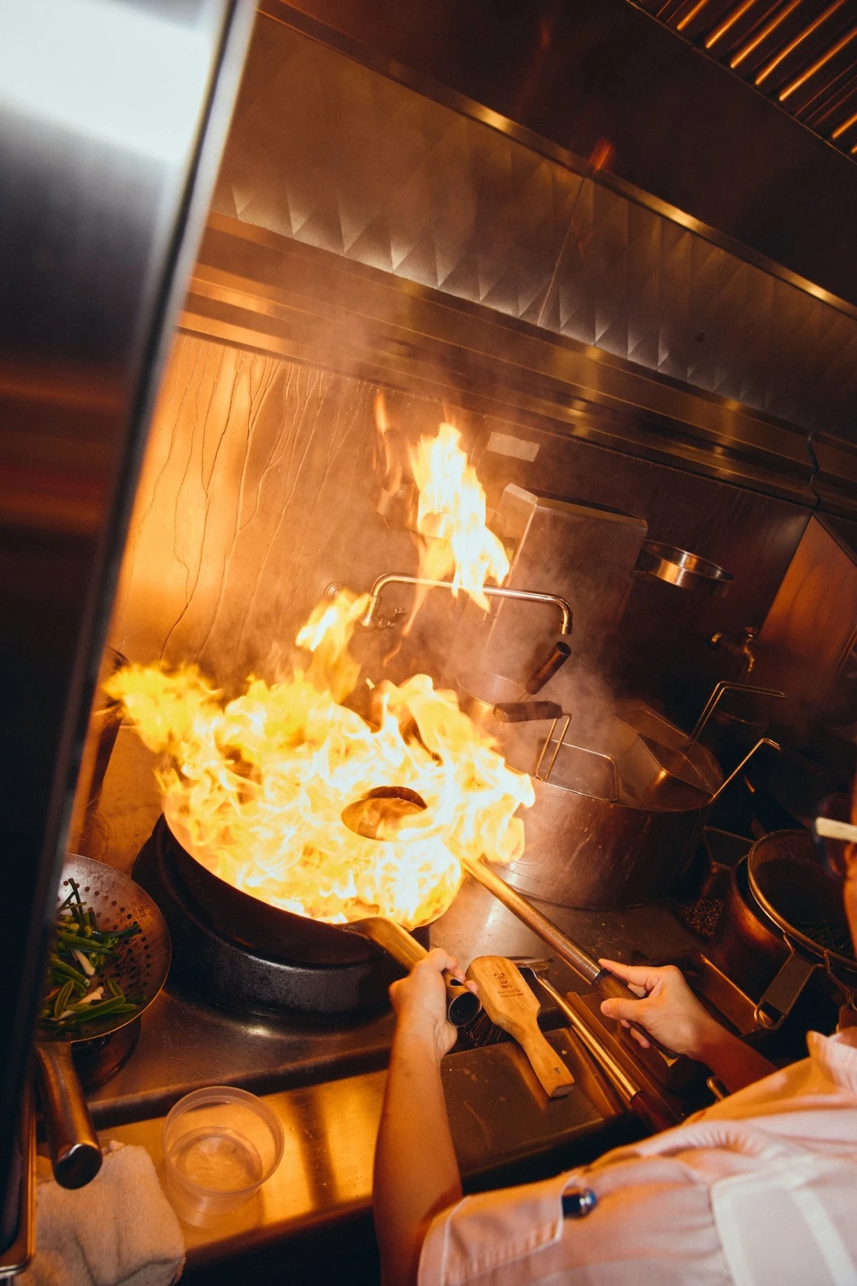 A chef performing wok cooking with dramatic flames in a professional kitchen; the source page explicitly attests this is from Mister Jiu's 10th annive
