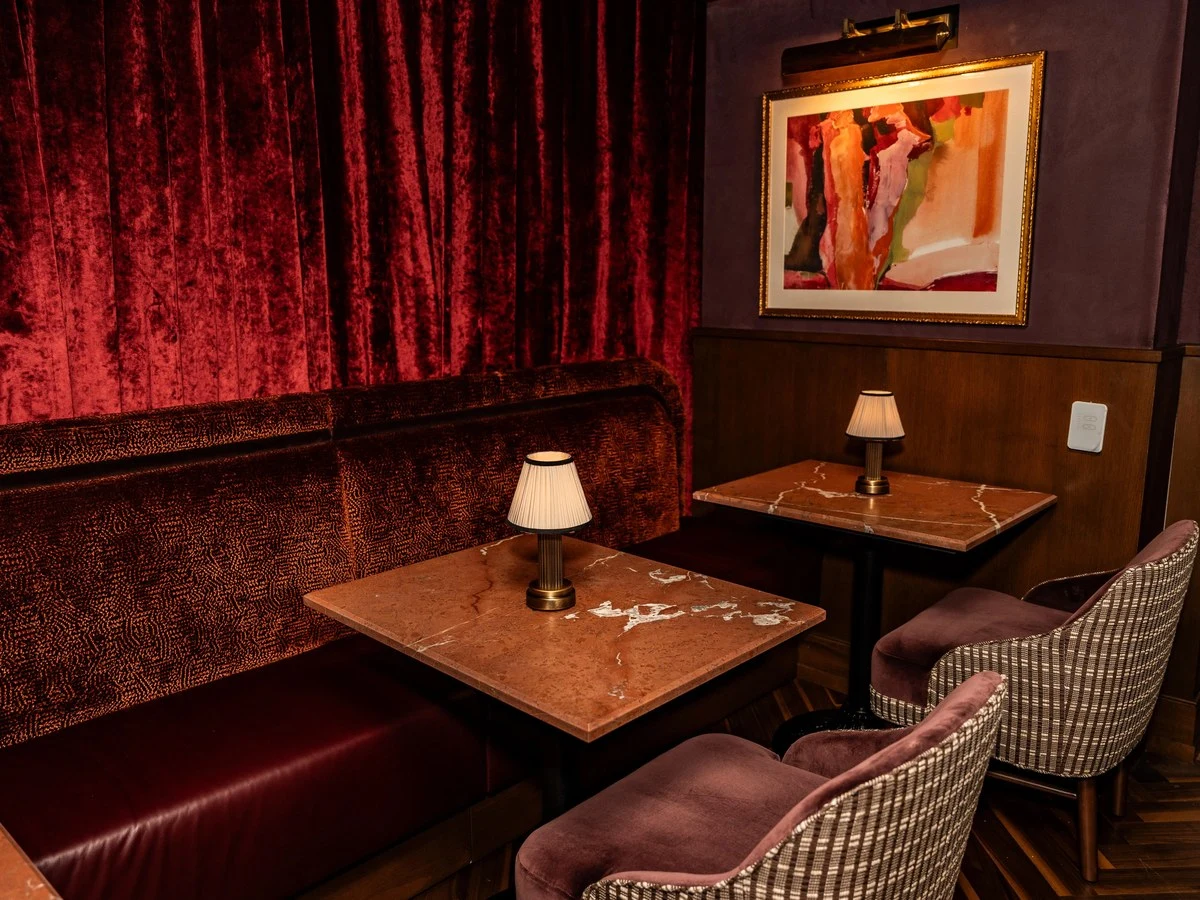 The Riggsby offers a moody dining nook with red velvet curtains, marble-top tables, and plush seating.
