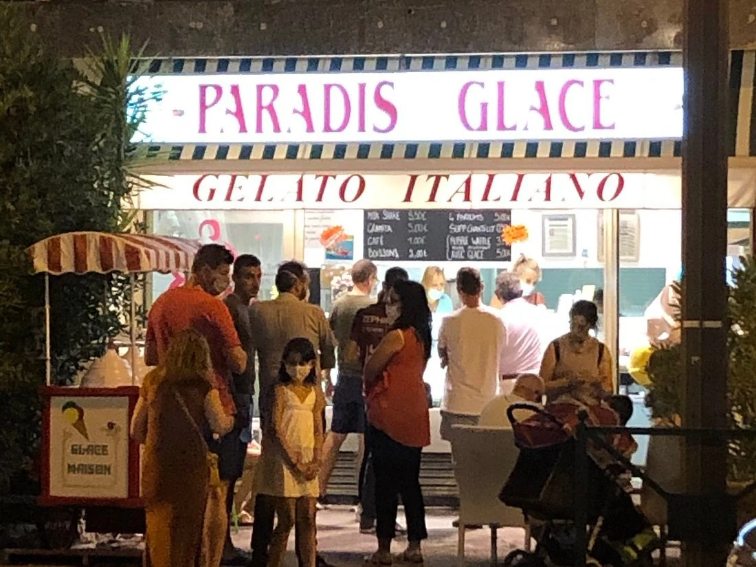 Gelato shop with customers in front of "Paradis Glace" sign at night.
