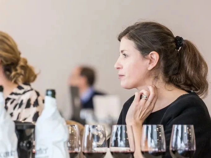 A woman with dark hair in a ponytail is seated at a wine tasting, with multiple wine glasses in front of her