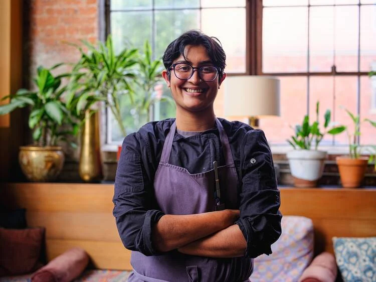 A person wearing glasses and a purple apron in a kitchen/restaurant setting with plants and windows; Time Out's editorial caption explicitly names thi