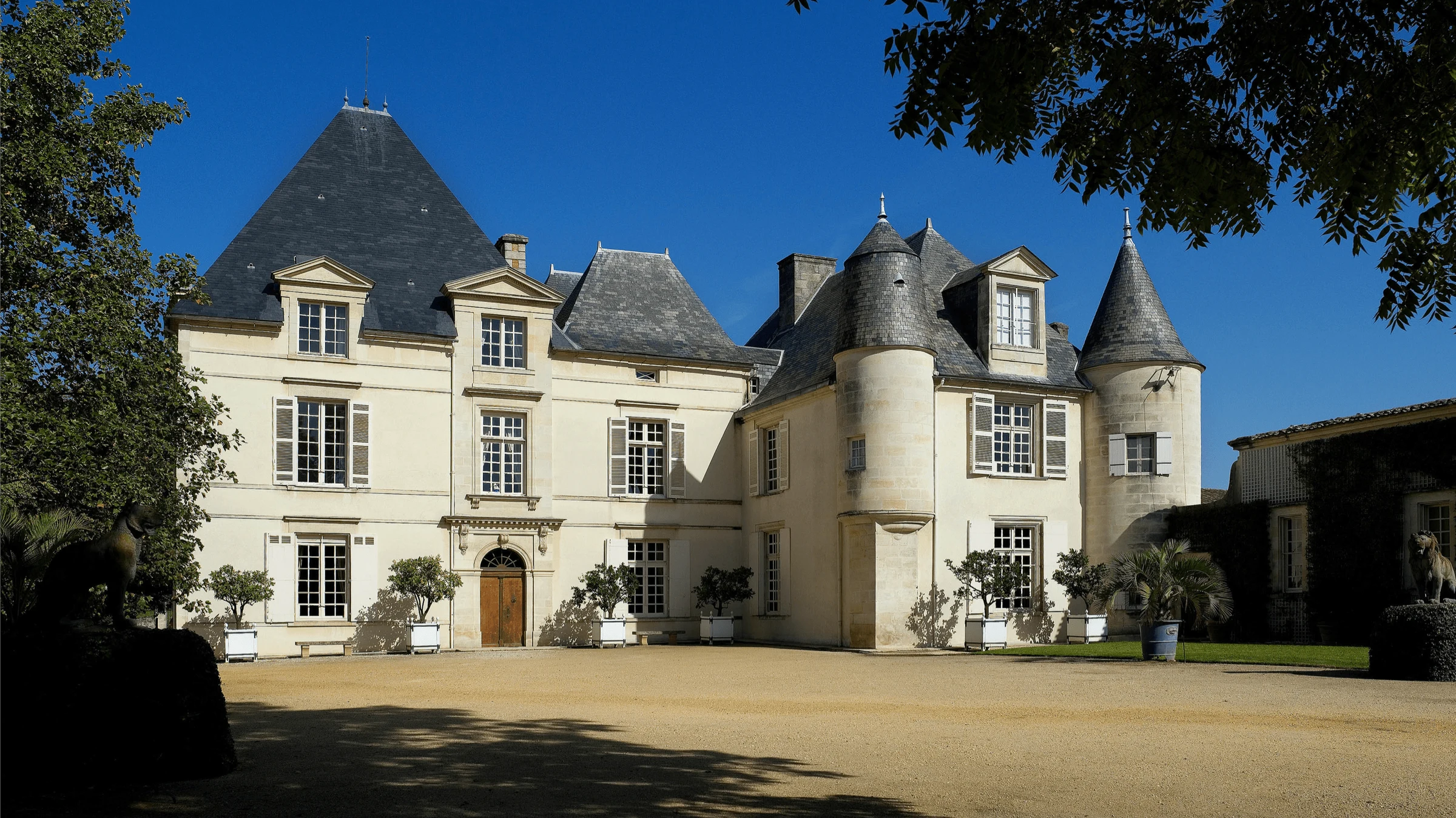 Château Haut-Brion features distinctive slate-grey turrets under a brilliant blue sky.