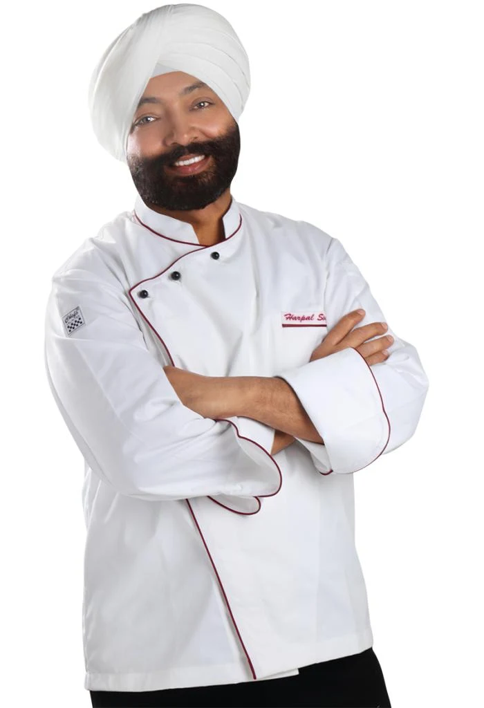 Professional portrait of a chef in white chef's coat with red piping wearing a white turban and beard, arms crossed in confident pose