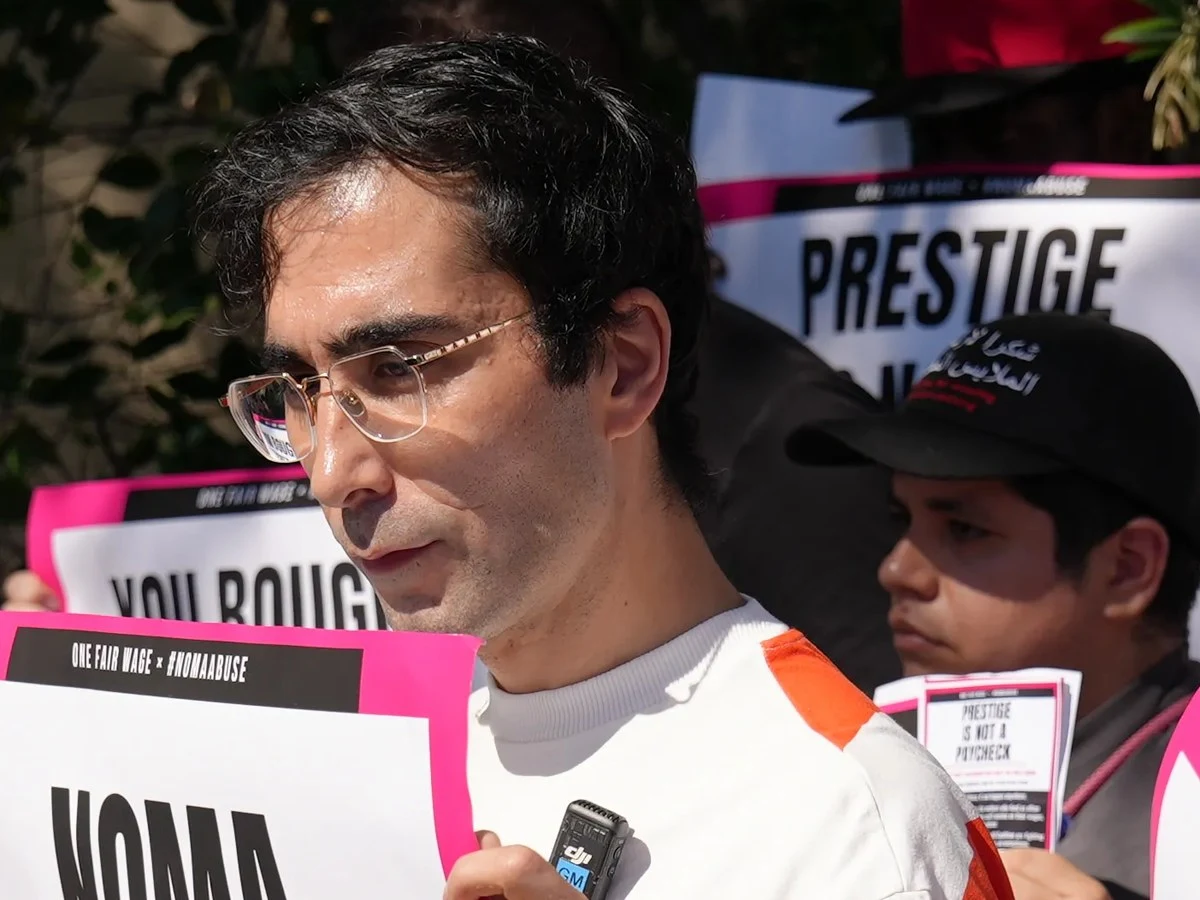 Jason Ignacio White leads a protest outside noma la residency, holding a sign reading "NOMA BROKE ME.