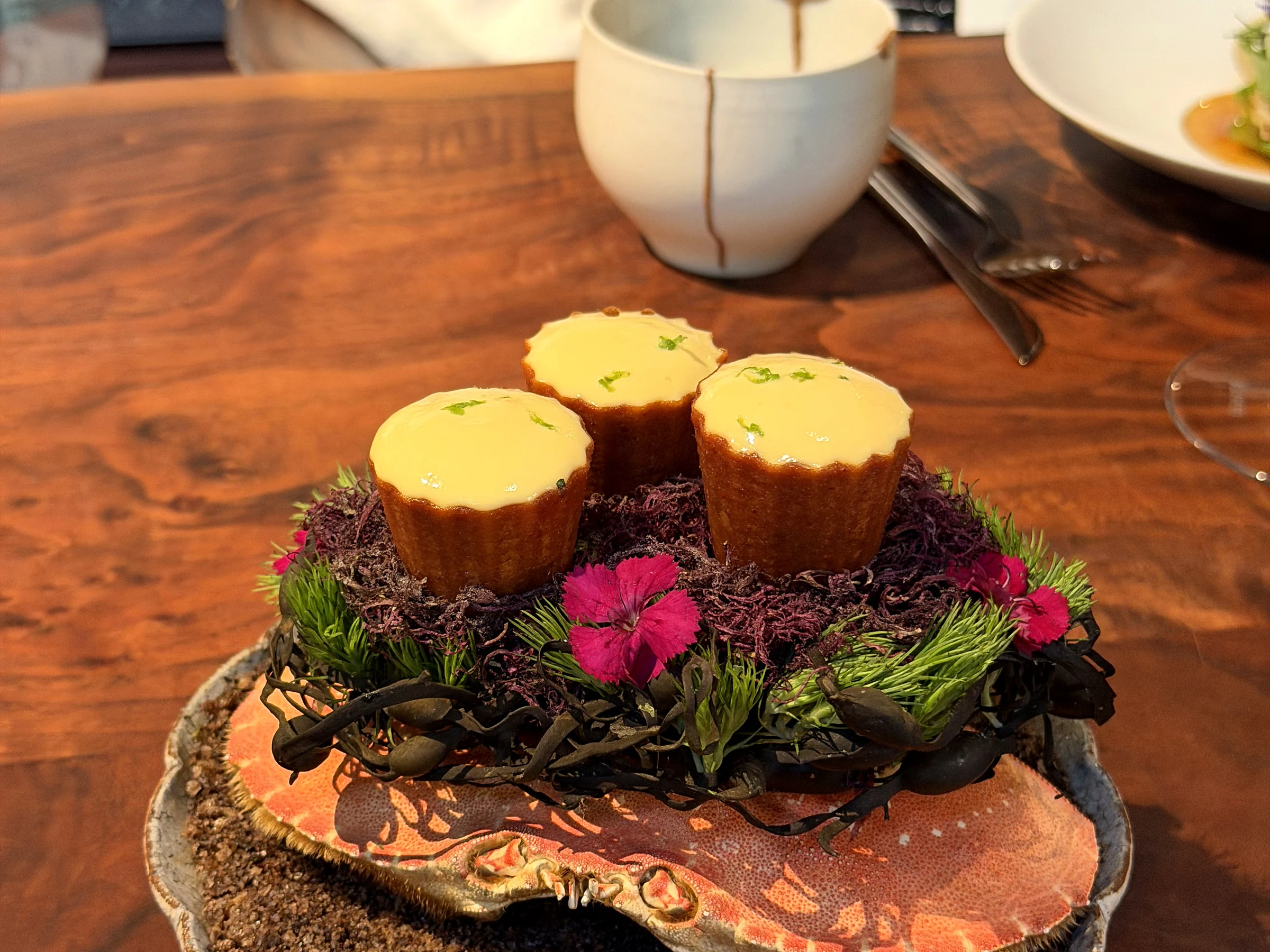 Composed Saison course presented with floral and seaweed garnishes on a sculptural platter