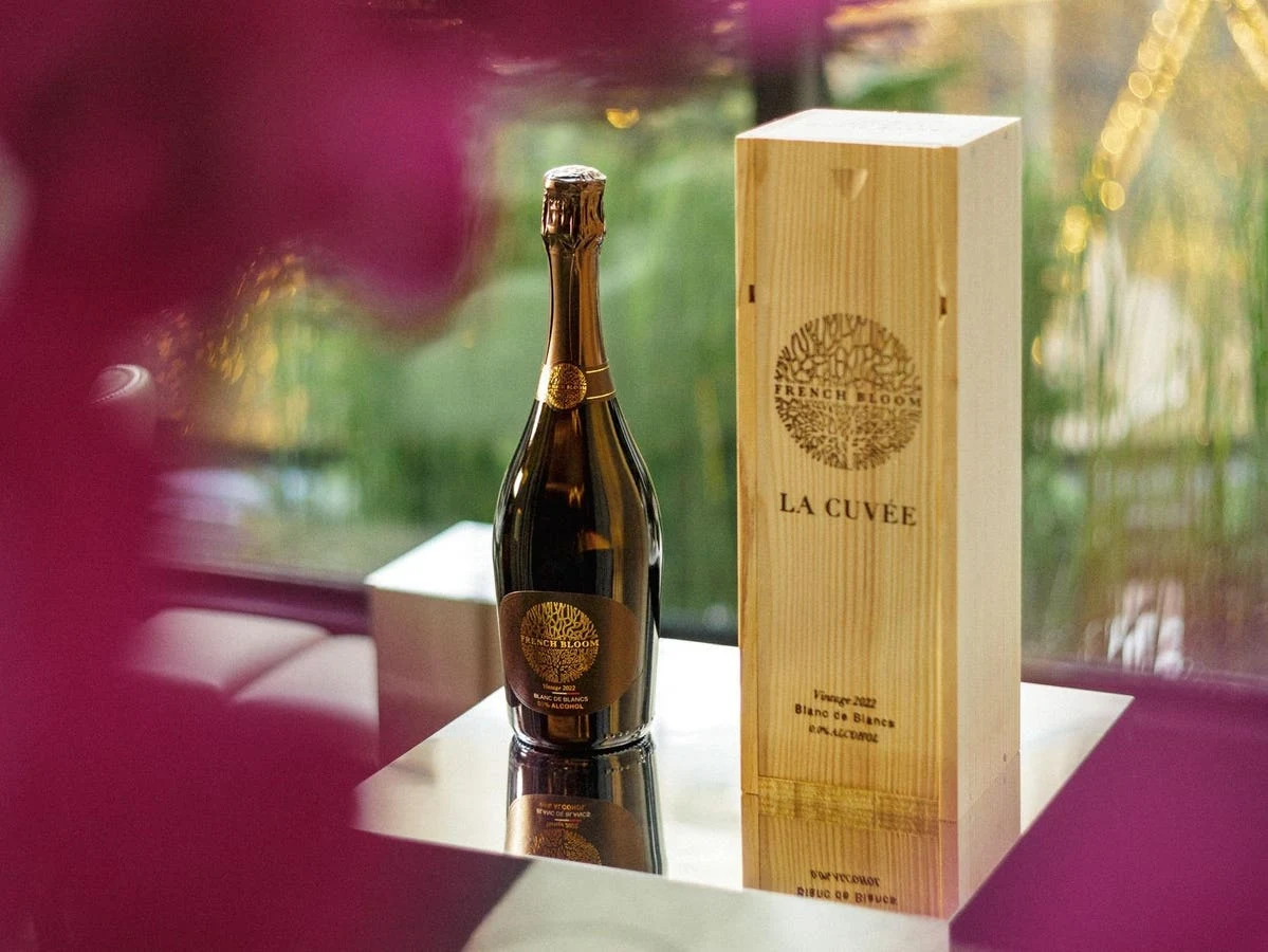 A French Bloom 'La Cuvée' bottle in dark glass with gold label alongside its wooden presentation box, photographed in an editorial product-detail styl