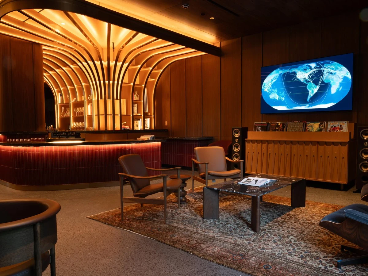 The Riggsby's lounge features an arched wood slat ceiling, red tiled bar, and a TV displaying a flight map.