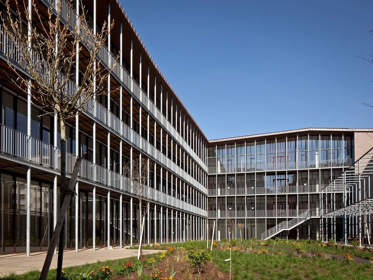 Exterior view of the Hermès atelier in Pantin, showing a modern multi-story building with a metal-and-glass facade and an inner courtyard garden.