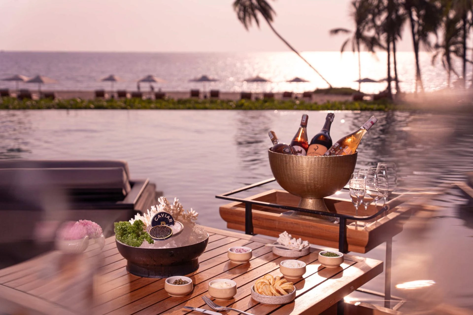 Beachfront dining terrace with infinity pool, champagne service setup, and ocean view