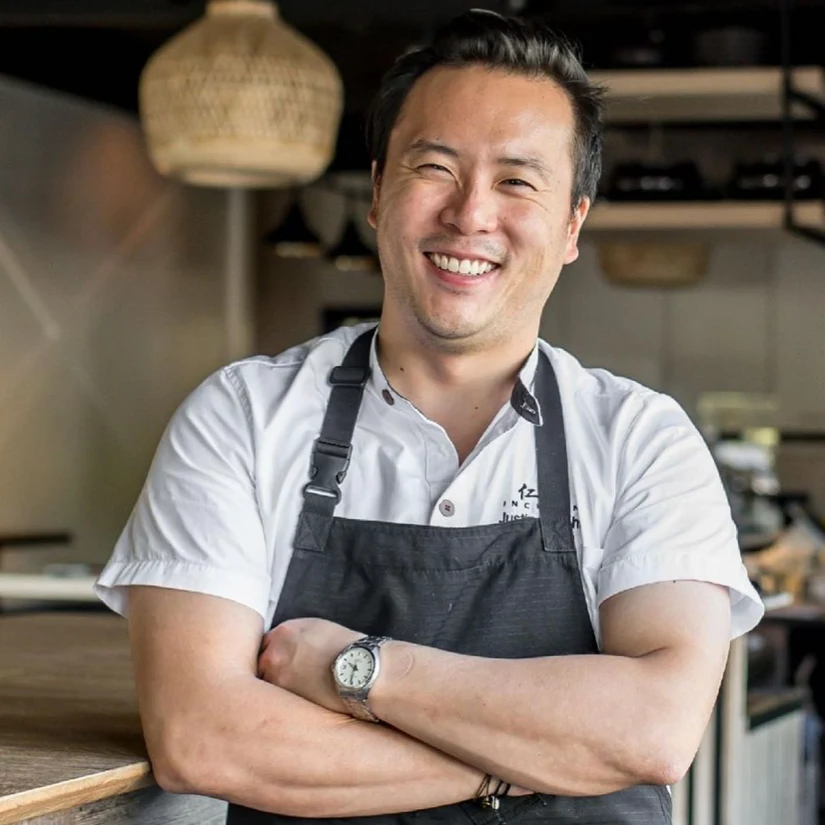 Portrait of a chef in a white chef's coat and dark apron standing in a professional kitchen