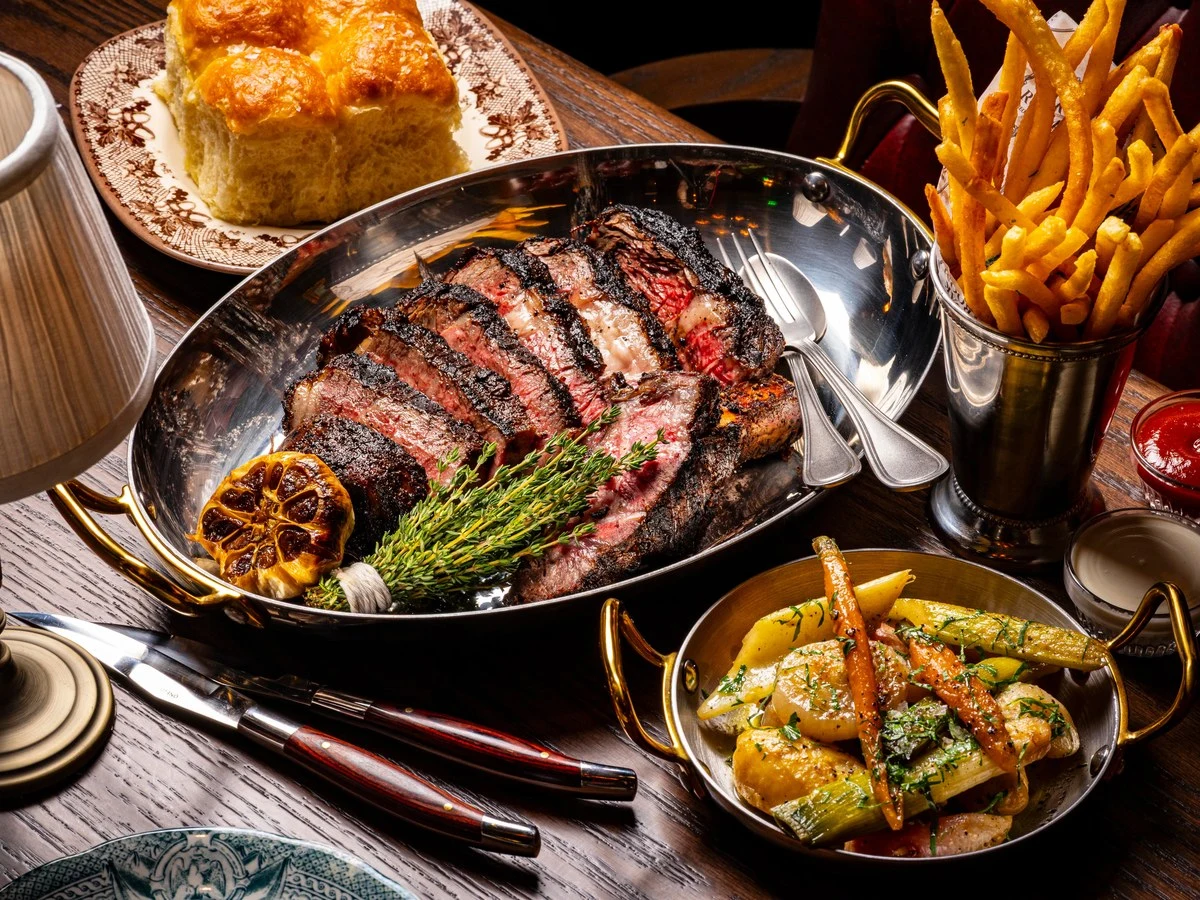 The Riggsby offers a delicious spread of steak, fries, roasted vegetables, and dinner rolls.