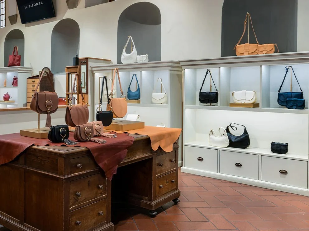 Interior of the Il Bisonte Florence shop, featuring vegetable-tanned leather handbags on white shelves and an antique wooden desk.
