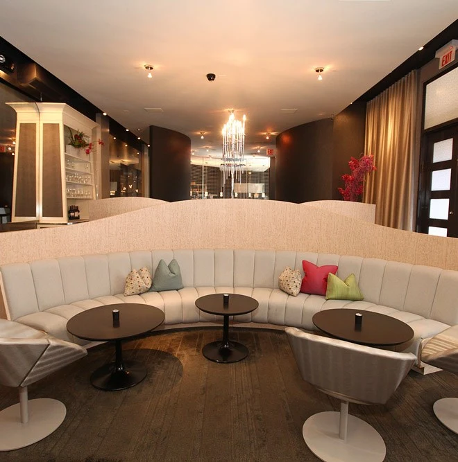 An upscale cocktail lounge interior with white curved banquette seating, small black pedestal tables, modern white swivel chairs, and a dramatic cryst