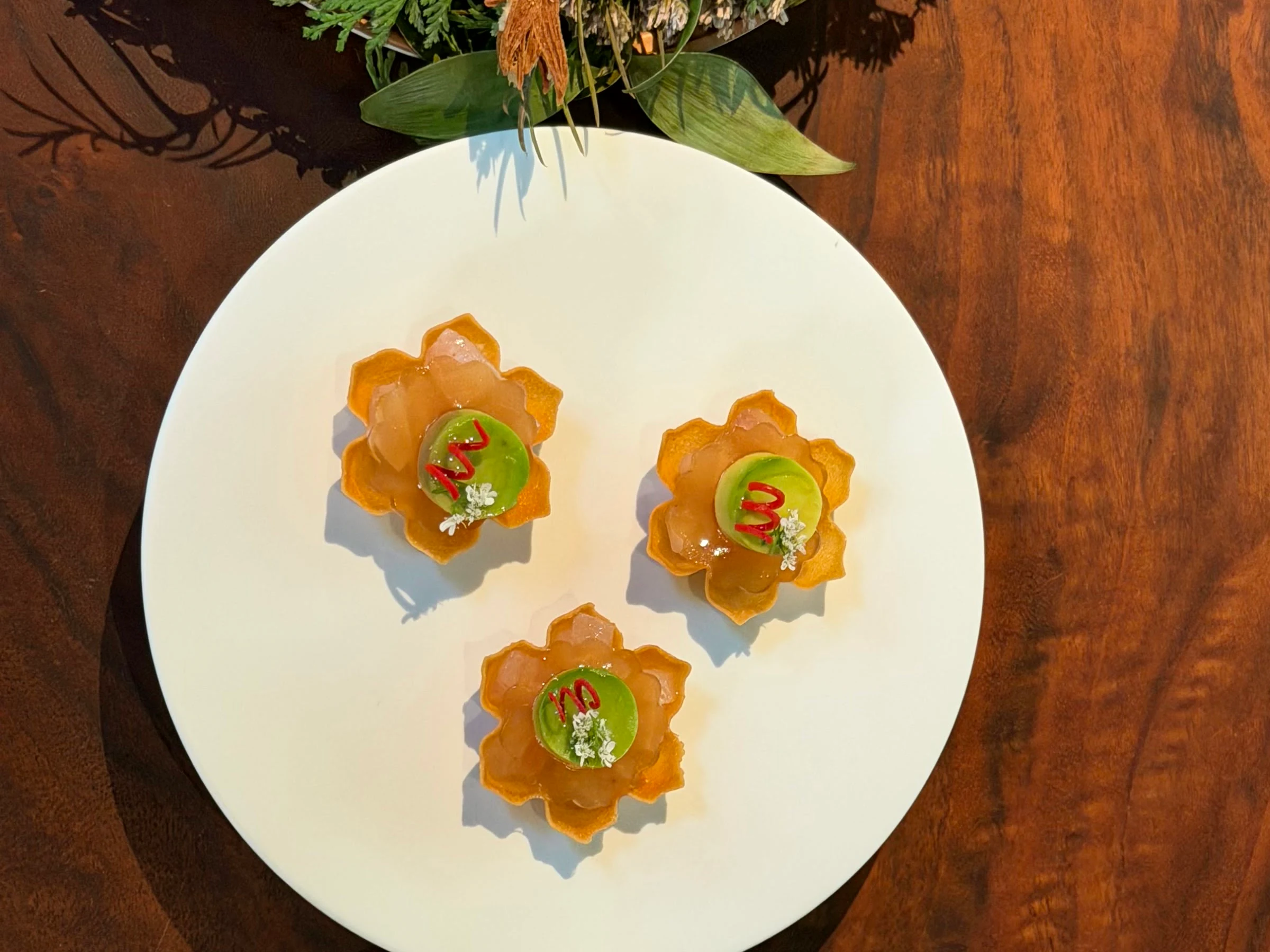 Three flower-shaped opening bites with green filling and fine garnishes on a white plate at Saison