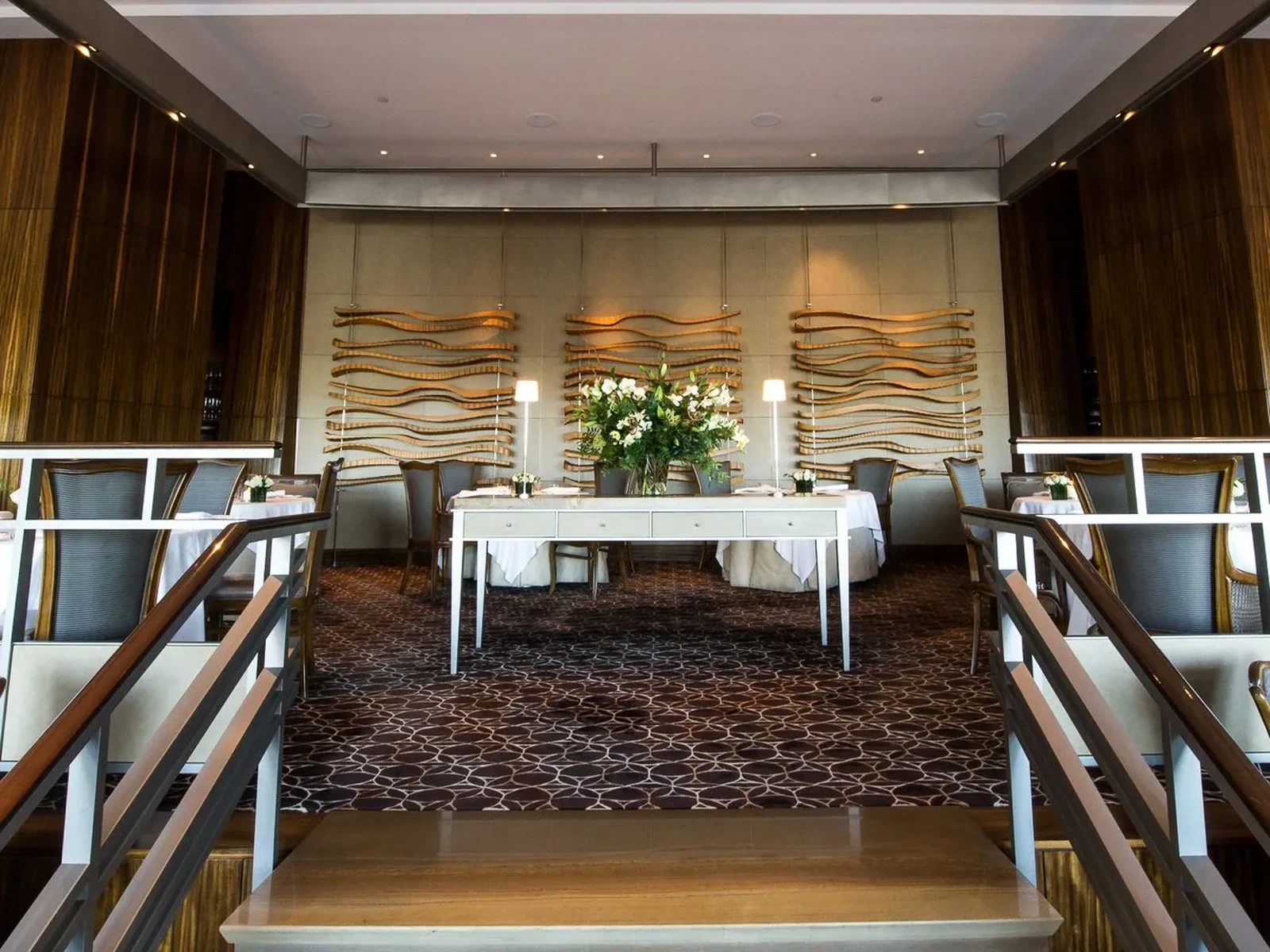 Restaurant dining room with tables, chairs, floral centerpiece, and gold wave wall art