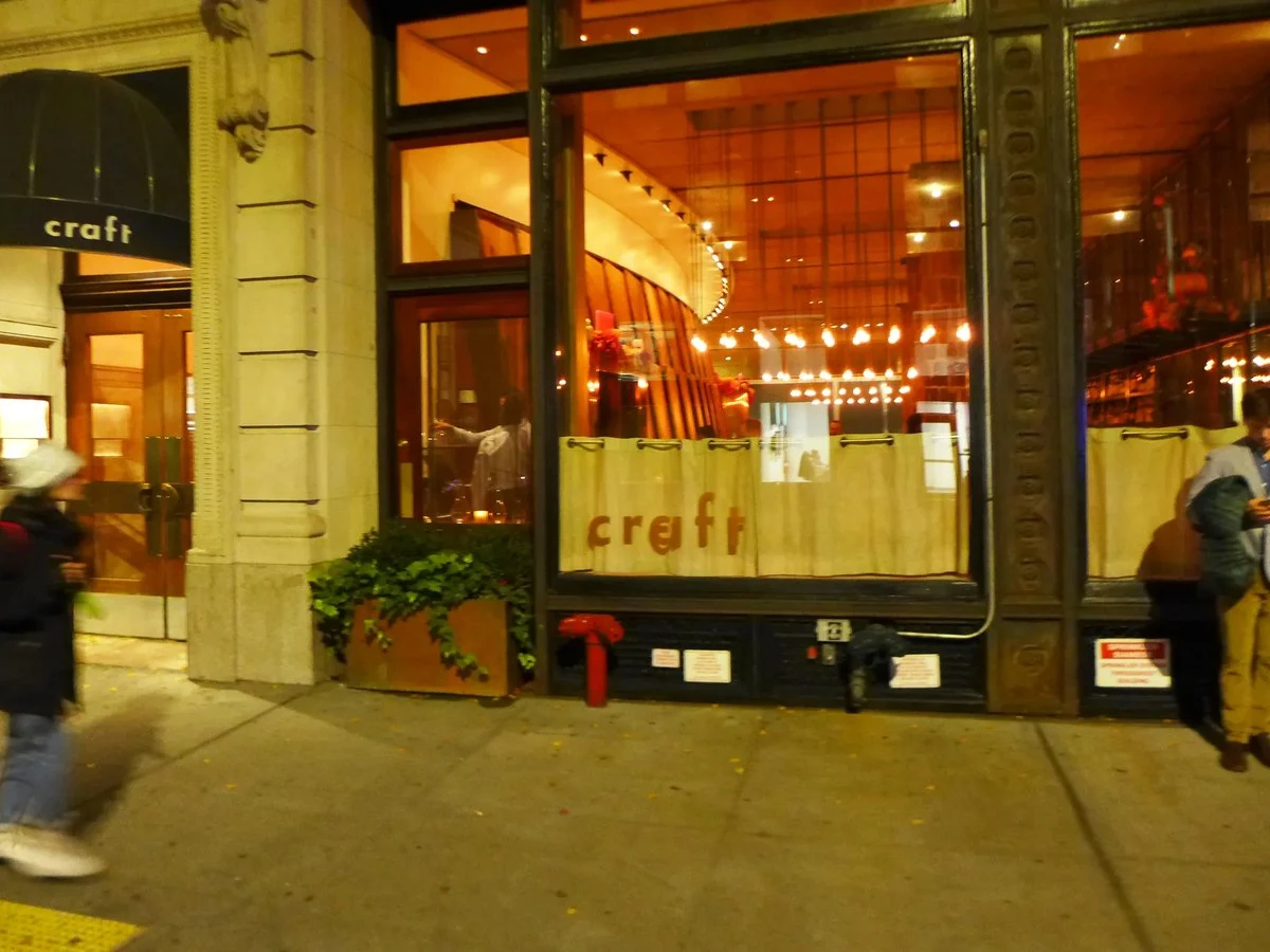 The exterior of Craft restaurant at night on East 19th Street, New York, with its awning and window signage visible.