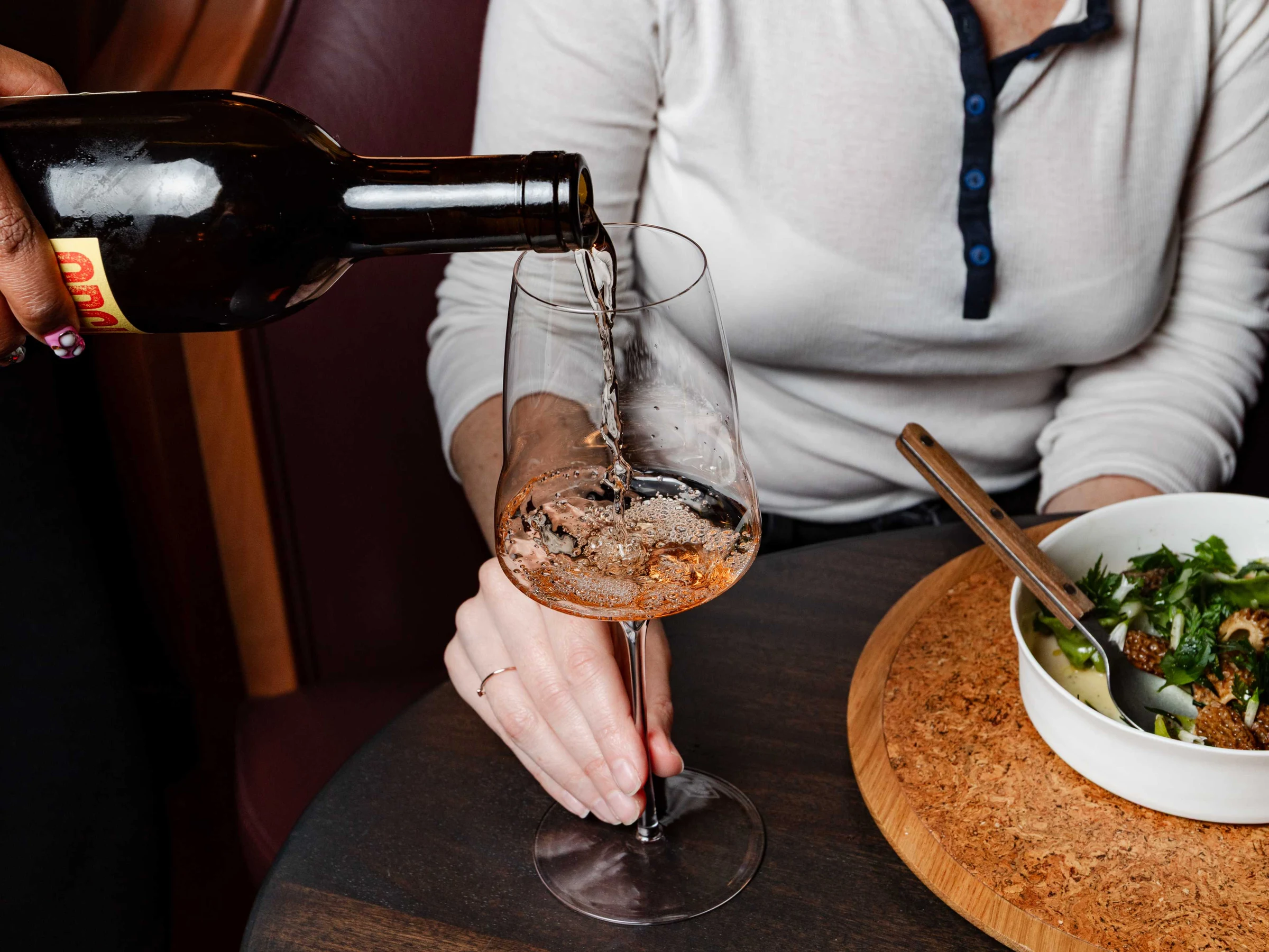 Lielle pours a glass of rosé wine at a restaurant table.