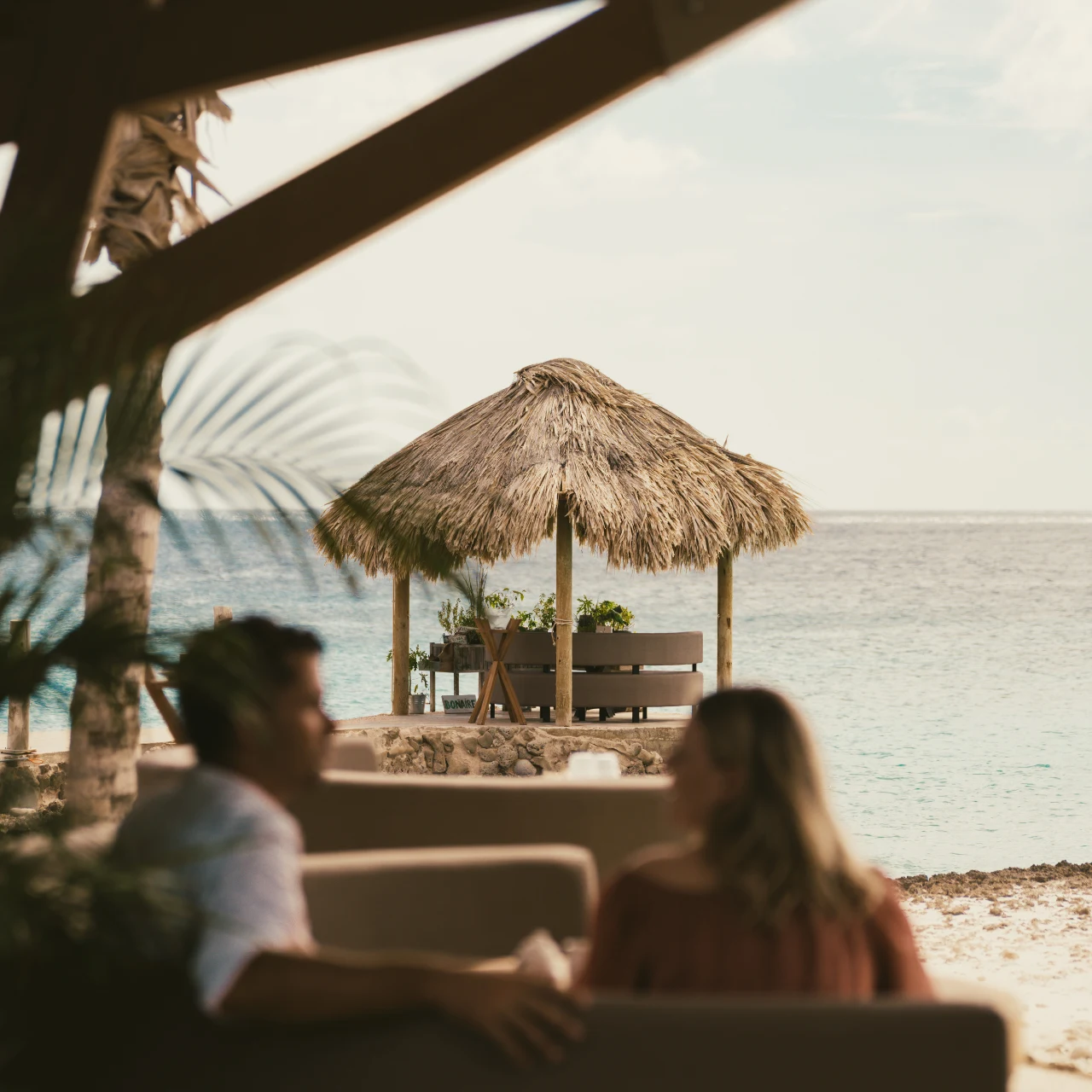 Open-air beachfront dining terrace with thatched palapa structures overlooking the Caribbean Sea
