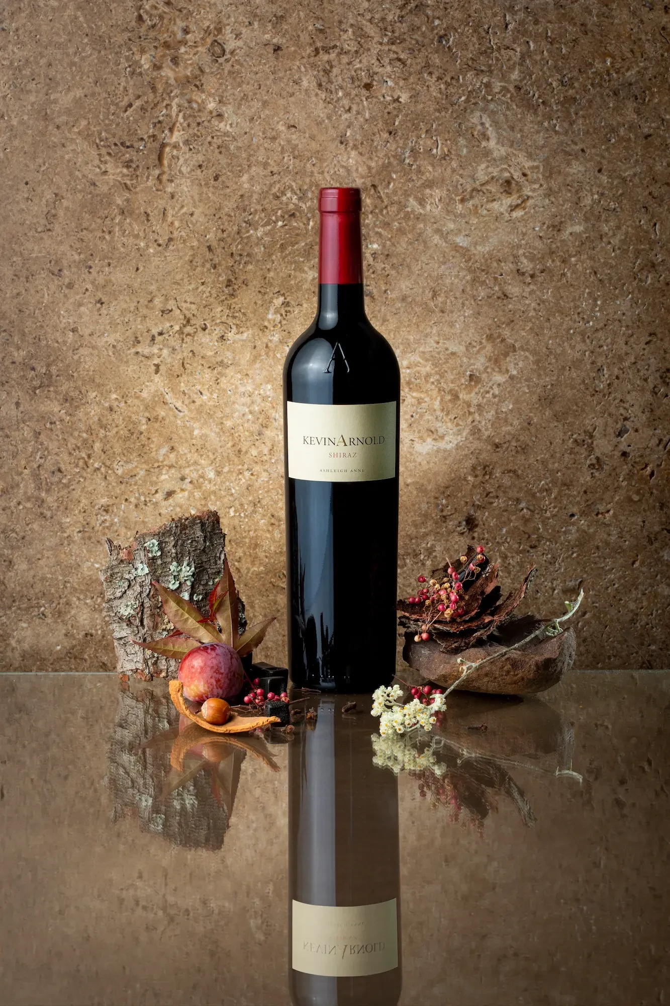 A bottle of Kevin Arnold Shiraz, central to Brian Tapera's journey, on a reflective surface with natural elements.
