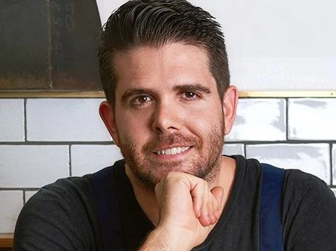 Adam Wolfers, chef and co-owner, at a wooden table in his restaurant.