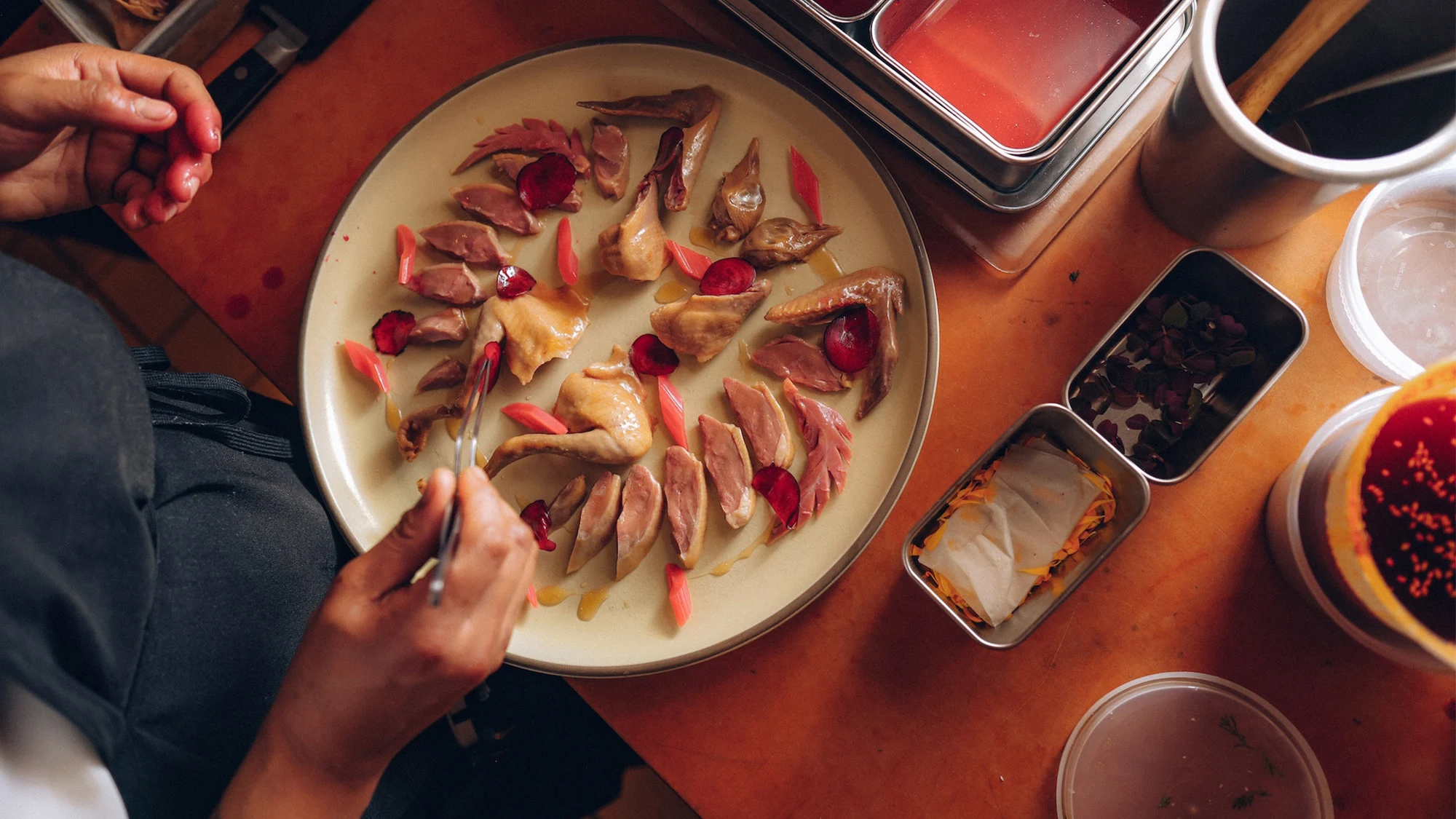 A plated dish of sliced duck with rose petals and curry sauce, photographed from above with hands arranging the presentation; the source page (Resy bl