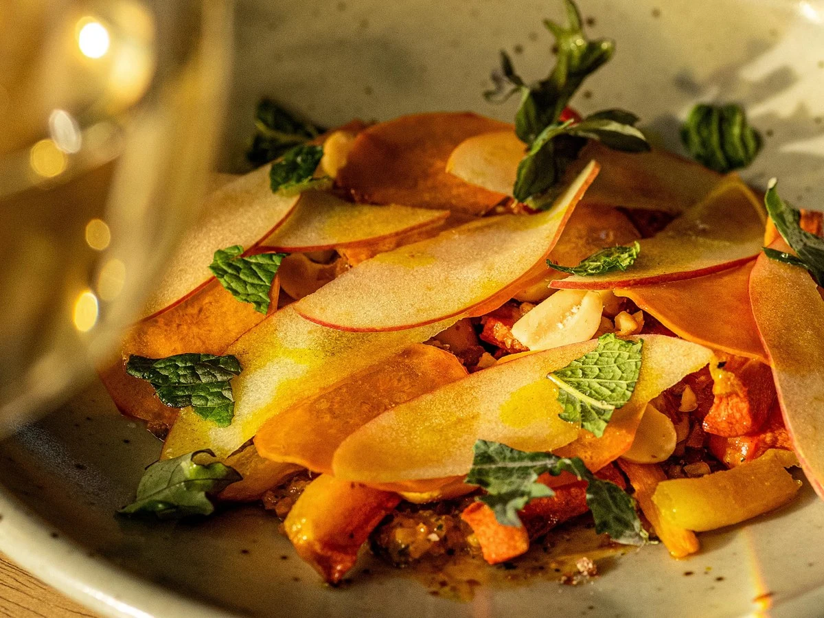 A close-up of a dish from Burnt Hill Farm's tasting menu, featuring thin slices of fruit, fresh mint leaves, and diced ingredients.