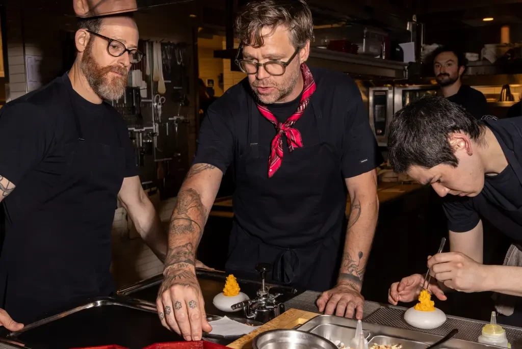 Professional kitchen scene showing chefs plating dishes with yellow garnishes in a commercial kitchen; the Los Angeles Times page title explicitly ide
