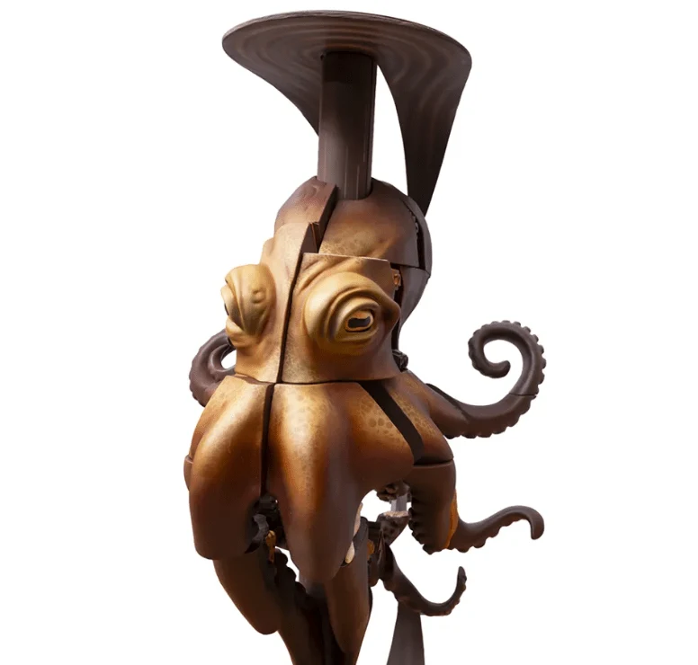 A chocolate sculpture of an octopus with a golden-bronze metallic body, dark brown tentacles with spiral curls, and a distinctive flared top resemblin