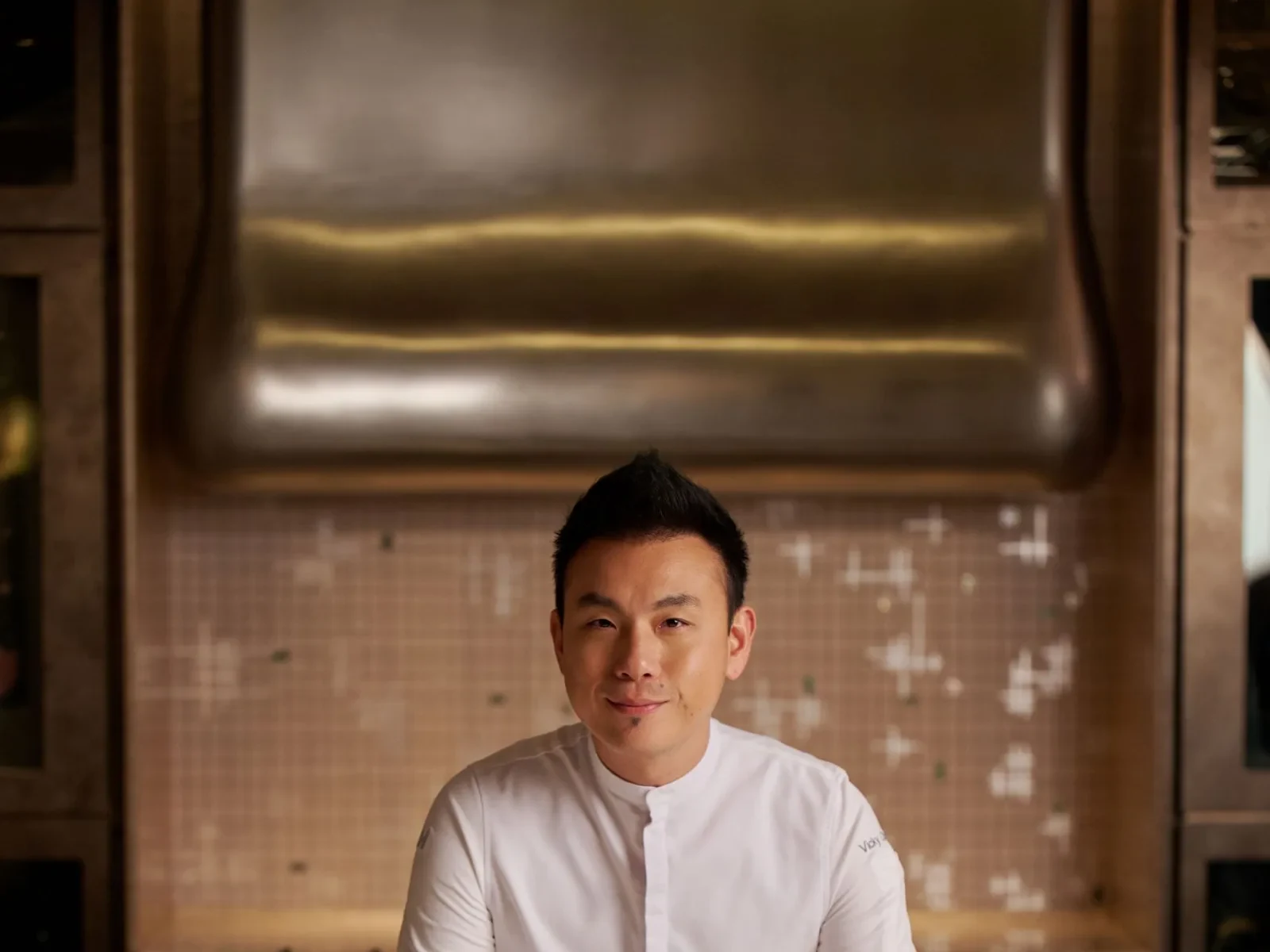 Chef in a modern kitchen with metallic accents and tiled background.