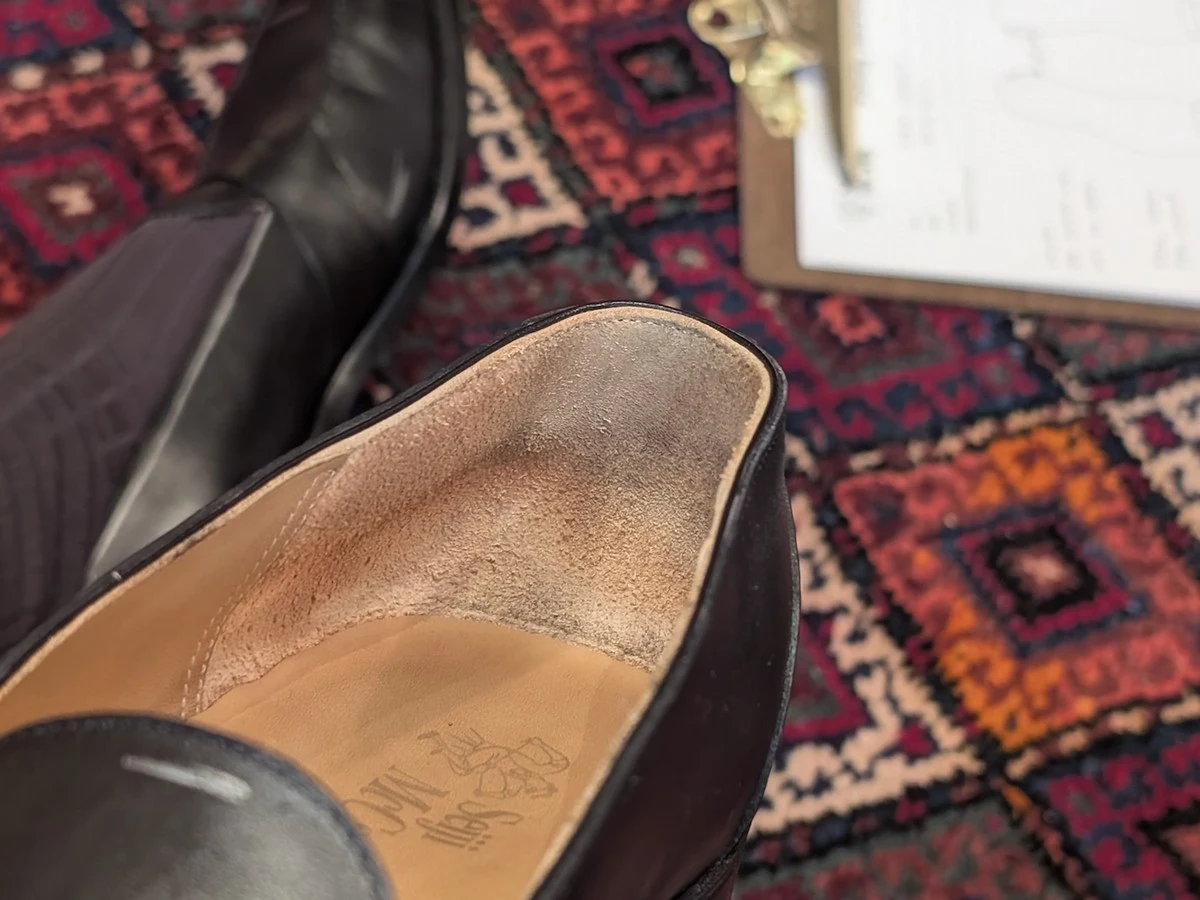 A close-up of a person's feet in black leather loafers on a patterned rug, with a clipboard nearby.