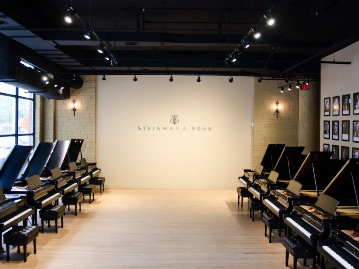 The Steinway Selection Center of Houston showcases rows of grand pianos, with the Steinway & Sons wordmark on the wall.