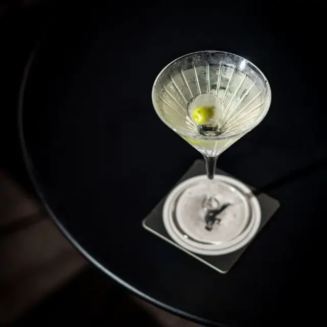 A bartender garnishes a martini with a citrus twist, creating a mist of aromatic oils over the drink.
