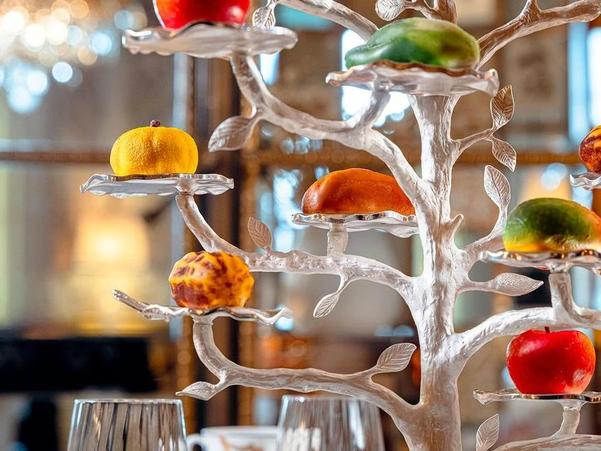 A trompe-l'oeil fruit sculpture dessert, presented on a striking silver tree stand.