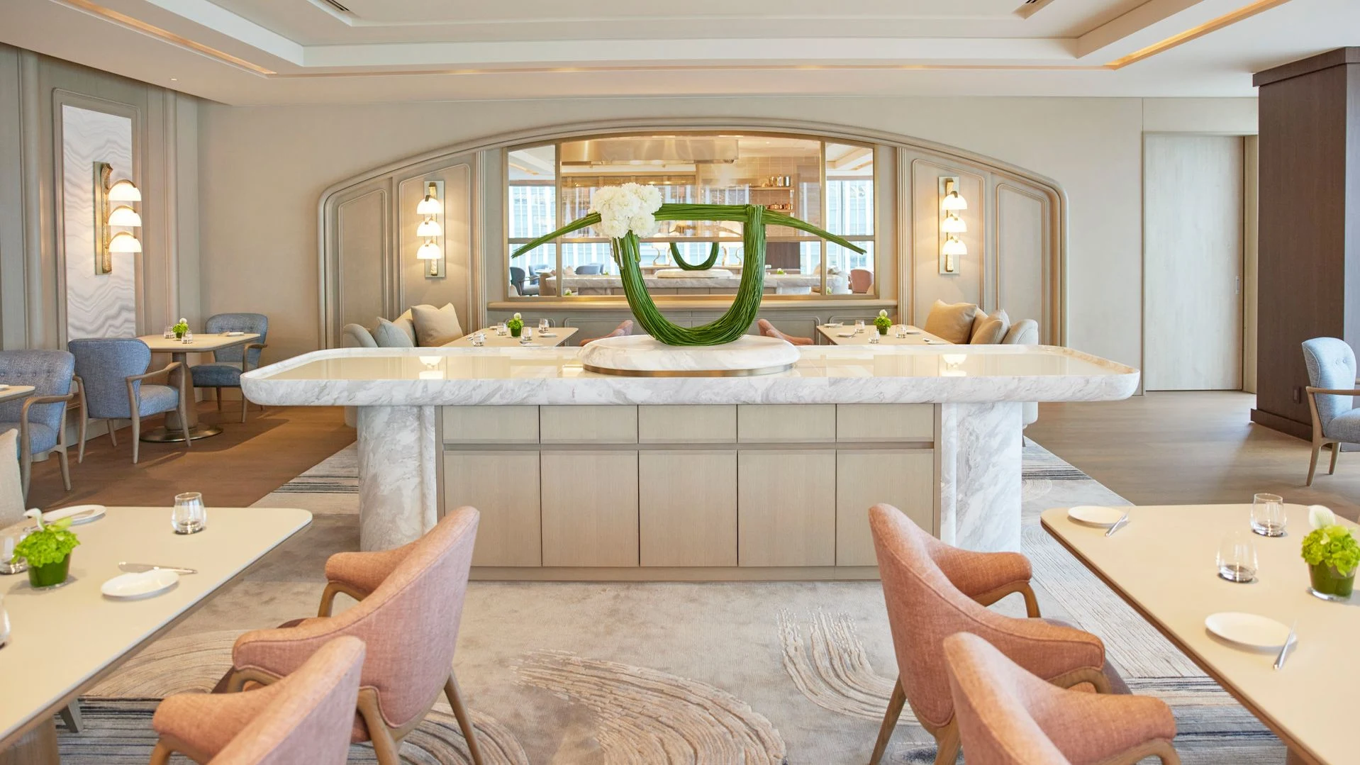 Sézanne's elegant dining room features coral-pink chairs, a white marble counter, and a striking green floral arrangement.