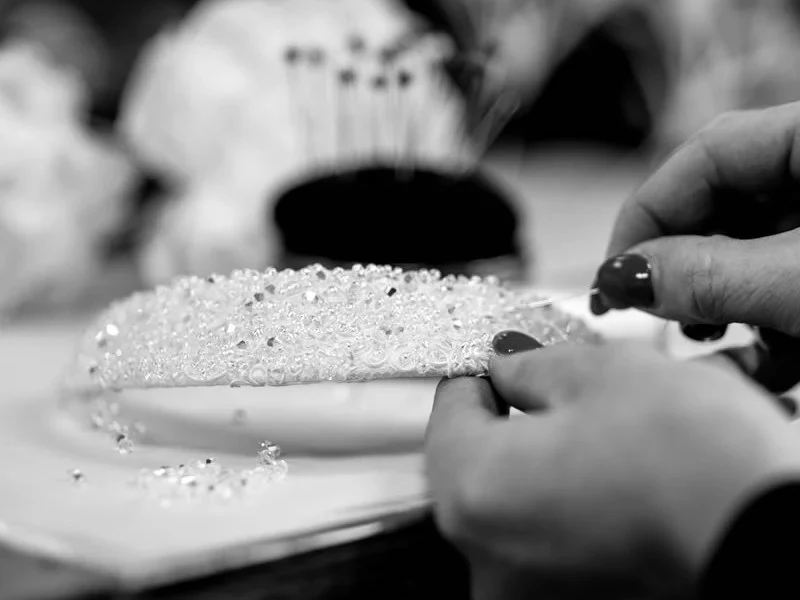 Close-up of hands with dark nail polish working on a heavily beaded and crystal-encrusted headpiece.