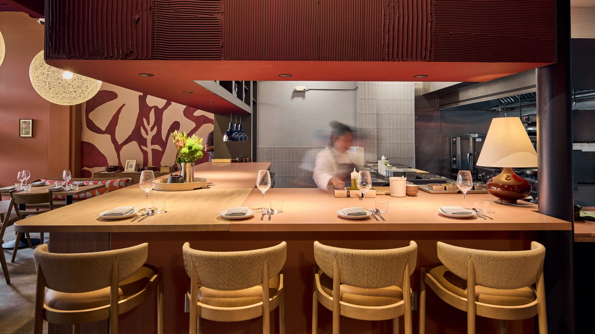 A four-seat chef's counter with place settings facing an open kitchen with a blurred chef in motion