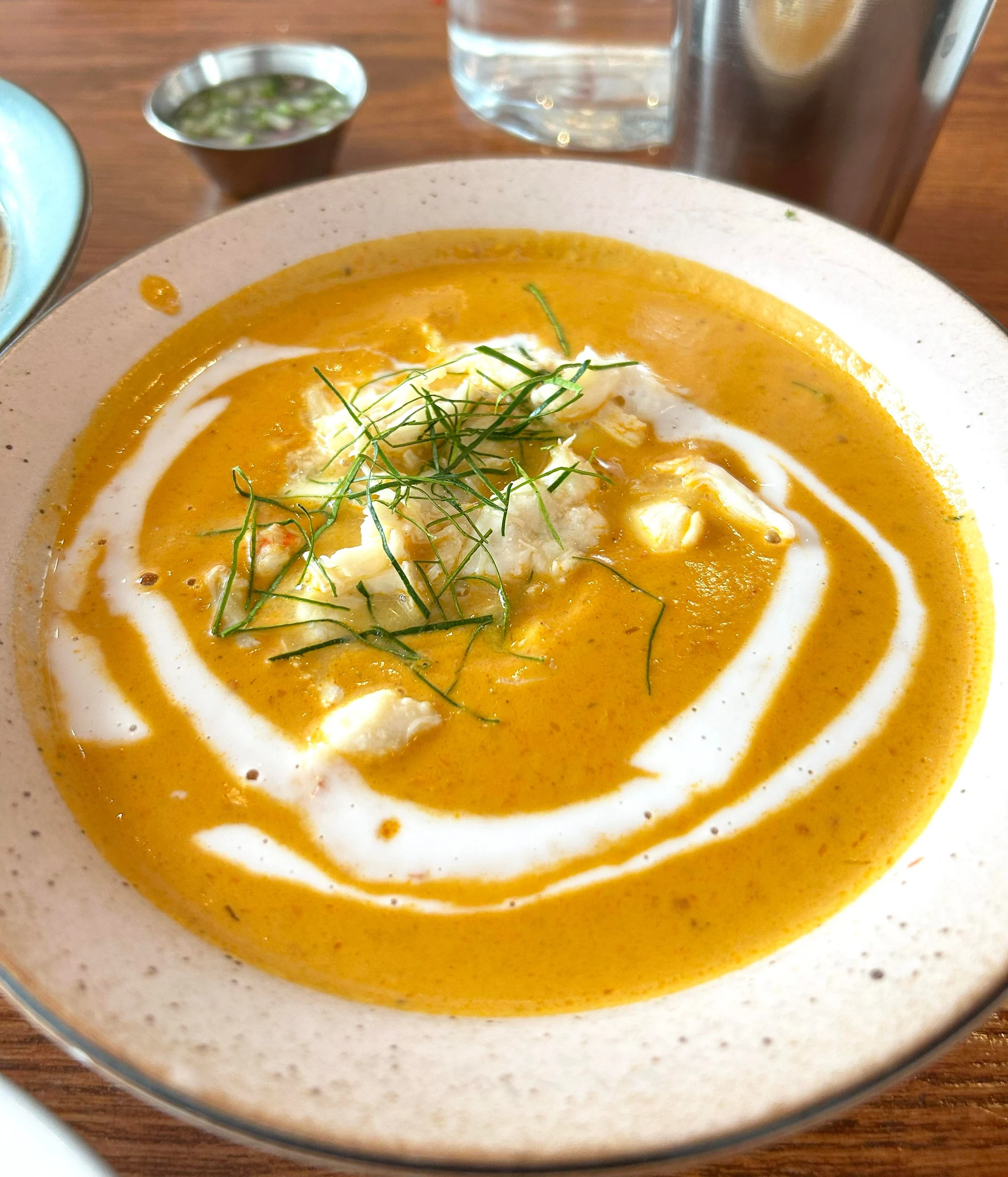 A beautifully plated soup dish with orange-yellow purée, cream swirl, crumbled cheese, and fresh dill garnish, photographed in a restaurant setting; t