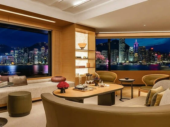 Upscale hotel lounge interior with floor-to-ceiling windows overlooking Victoria Harbour's illuminated Hong Kong skyline at night, featuring curved se