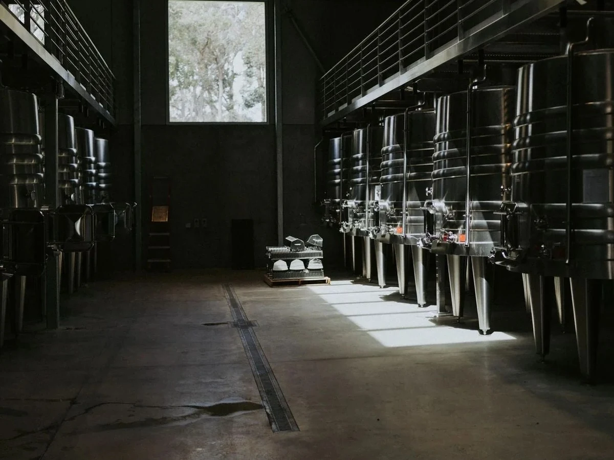 A modern winery interior with rows of tall, gleaming stainless steel fermentation tanks on both sides of a central aisle.