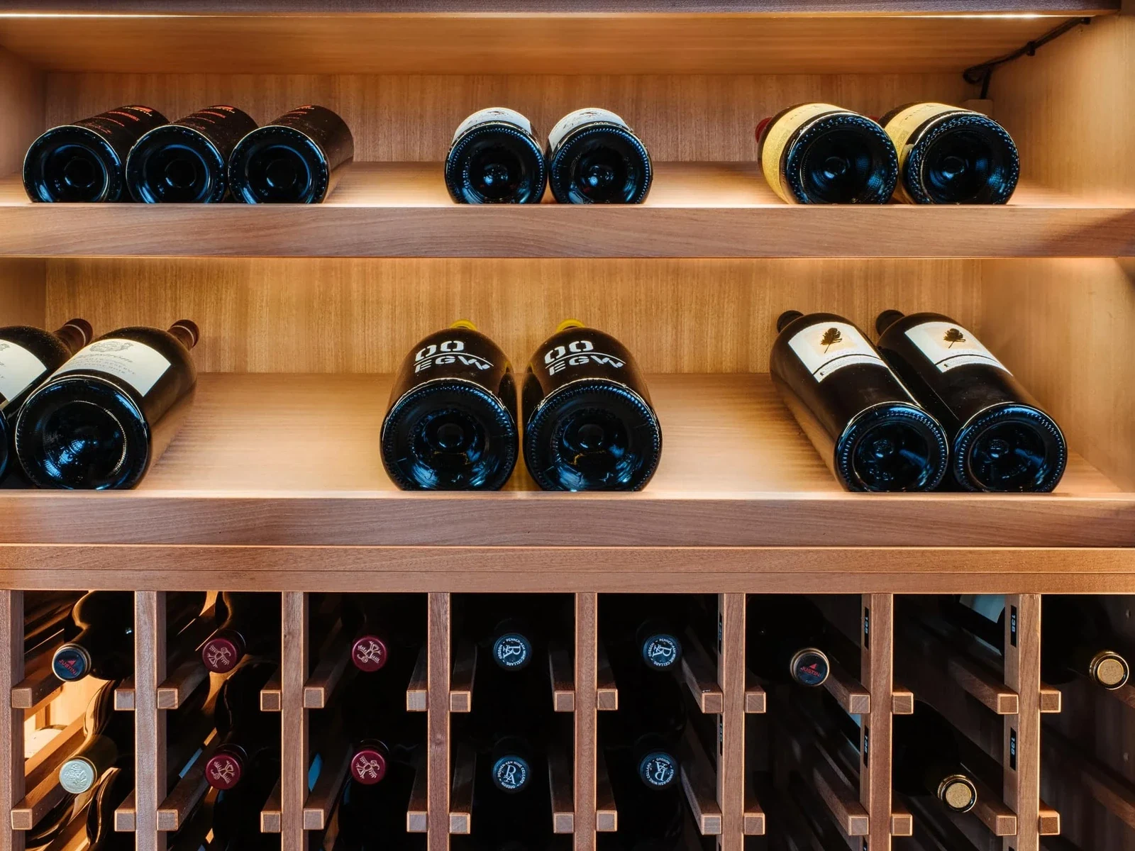 Wooden wine rack with bottles stored horizontally on illuminated shelves and in individual cubbies below